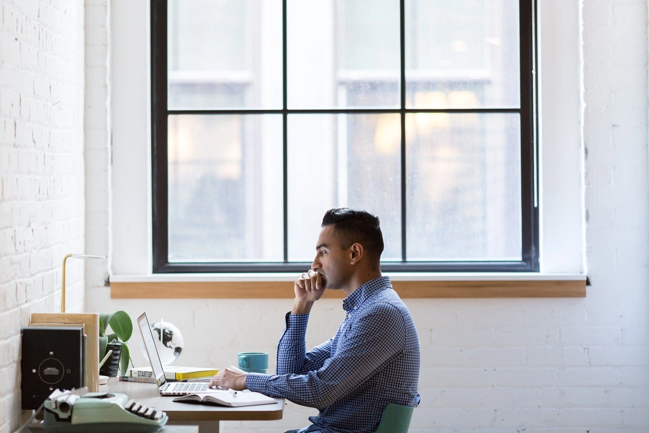 The interior of an architecture studio. A 3d designer is sitting at a computer with a window behind.