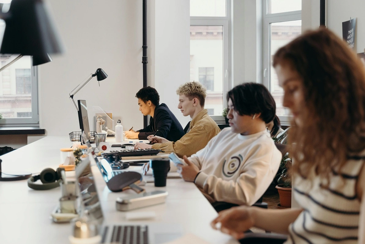 3D designers sitting at a white table, working on their computers and doing 3D renders.